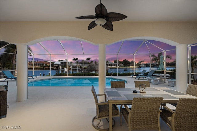 outdoor pool with a patio area, glass enclosure, a water view, and ceiling fan