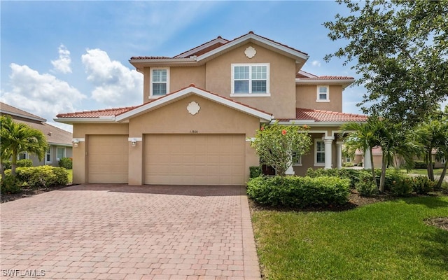 mediterranean / spanish home with decorative driveway, stucco siding, a tile roof, a front lawn, and an attached garage