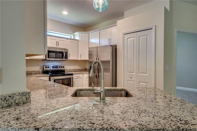 kitchen with stainless steel appliances, light stone counters, white cabinetry, and a sink