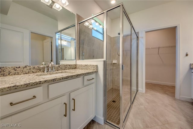 full bath with a walk in closet, vanity, tile patterned floors, baseboards, and a shower stall