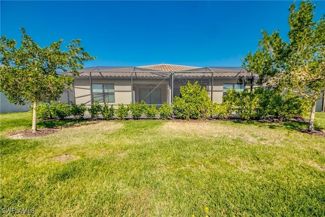 rear view of house with a lawn, glass enclosure, stucco siding, and a tiled roof