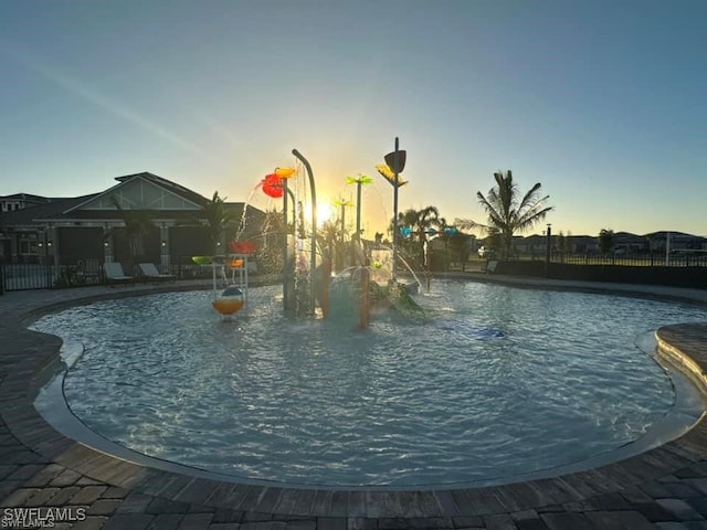 pool at dusk featuring a community pool and fence