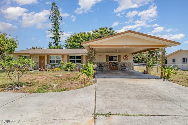 view of front of home with stone siding, fence, concrete driveway, and an attached carport