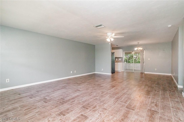 spare room with baseboards, ceiling fan with notable chandelier, light wood-type flooring, and visible vents