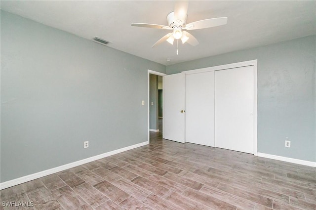 unfurnished bedroom featuring wood finished floors, a closet, visible vents, baseboards, and ceiling fan