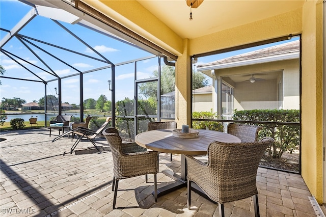 view of patio featuring a water view, outdoor dining area, glass enclosure, and ceiling fan