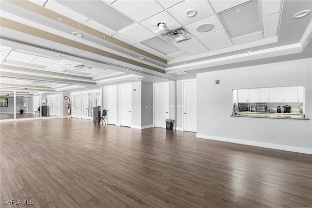 unfurnished living room featuring visible vents, baseboards, a tray ceiling, and dark wood-style floors