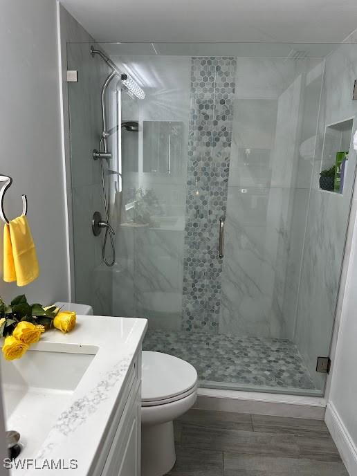 bathroom with toilet, baseboards, a shower stall, and vanity
