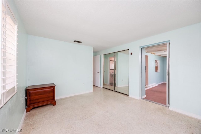 unfurnished bedroom with baseboards, visible vents, speckled floor, and a closet