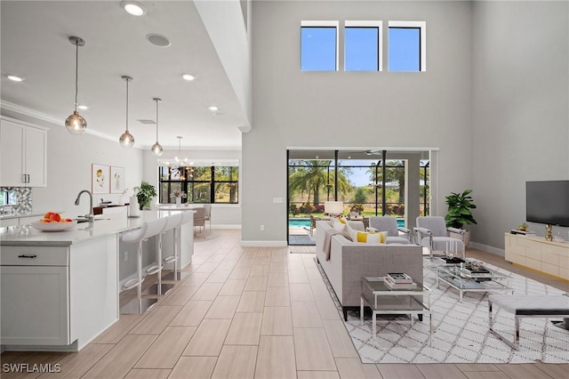 living area featuring crown molding, a notable chandelier, recessed lighting, baseboards, and a towering ceiling
