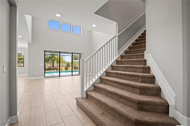 stairway with baseboards, tile patterned flooring, a high ceiling, and recessed lighting