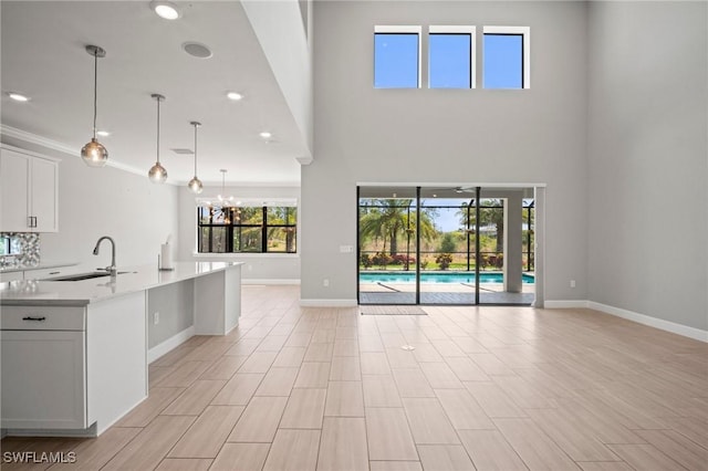 unfurnished living room featuring baseboards, a high ceiling, recessed lighting, a sink, and a notable chandelier