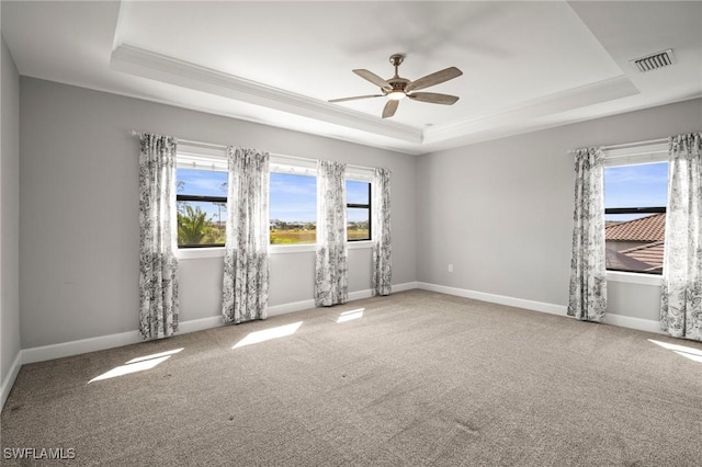 unfurnished room featuring a raised ceiling, ceiling fan, carpet, and visible vents