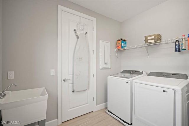 laundry area featuring washer and dryer, laundry area, a sink, light wood-style floors, and baseboards