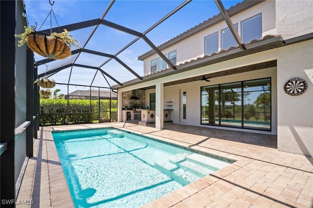 pool featuring glass enclosure, exterior kitchen, a ceiling fan, and a patio area