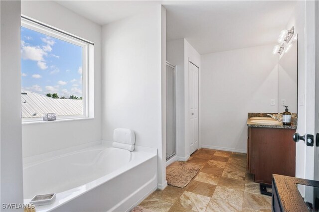 full bathroom featuring stone finish flooring, a bath, vanity, baseboards, and a stall shower