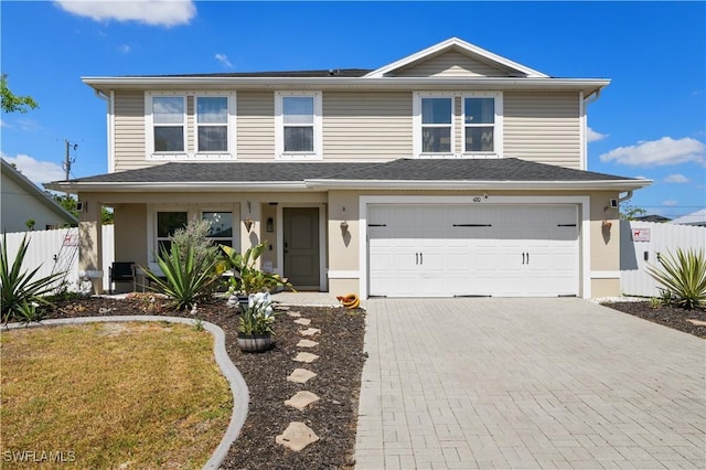 traditional-style house with decorative driveway, an attached garage, stucco siding, and fence