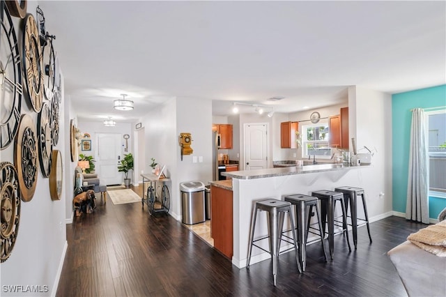 kitchen featuring wood finished floors, a breakfast bar area, light countertops, brown cabinets, and a peninsula