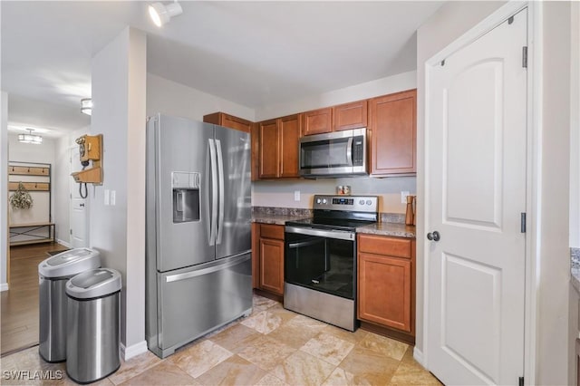 kitchen with stainless steel appliances, brown cabinetry, and baseboards