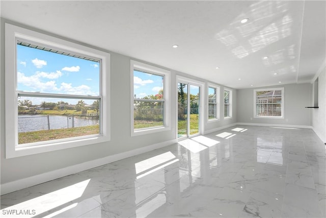 unfurnished living room with a healthy amount of sunlight, a water view, and baseboards