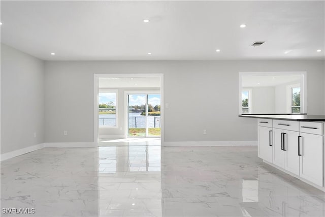 unfurnished living room with baseboards, visible vents, plenty of natural light, and marble finish floor