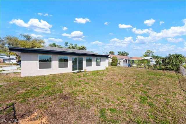 back of property featuring fence, stucco siding, and a lawn