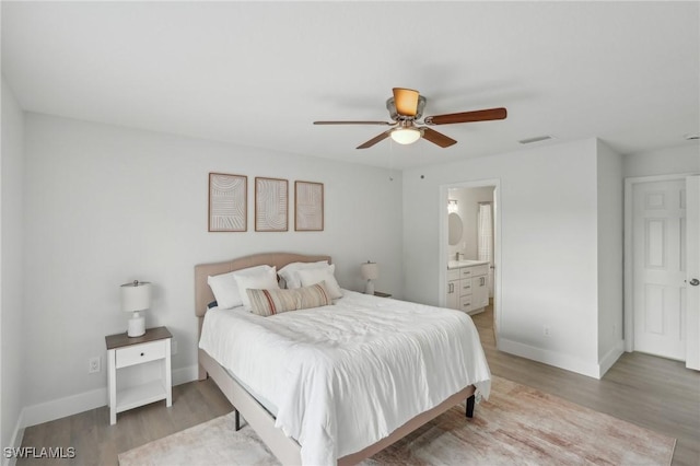 bedroom featuring baseboards, ensuite bath, wood finished floors, and visible vents