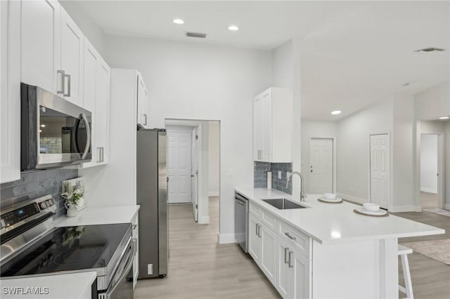 kitchen featuring visible vents, a peninsula, a kitchen bar, a sink, and appliances with stainless steel finishes