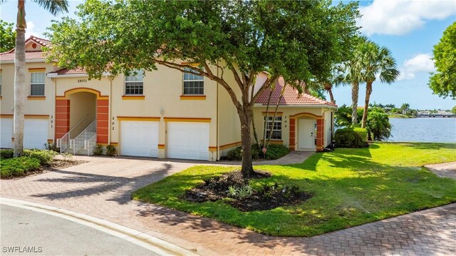 25073 Peacock Ln Unit 102, Naples, FL 34114 - view of front facade featuring an attached garage, a water view, a front lawn, driveway, and stucco siding
