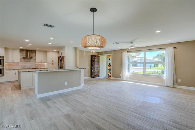 kitchen featuring visible vents, decorative backsplash, baseboards, wall chimney range hood, and a center island