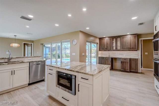 kitchen featuring stainless steel dishwasher, visible vents, glass insert cabinets, and a sink