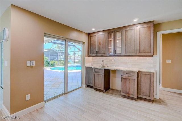 bar featuring baseboards, decorative backsplash, light wood-style flooring, and a sink