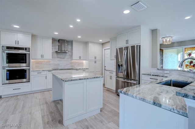 kitchen with wall chimney range hood, a sink, stainless steel appliances, a kitchen island, and visible vents