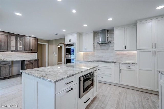 kitchen with decorative backsplash, light stone countertops, wall chimney range hood, recessed lighting, and stainless steel appliances