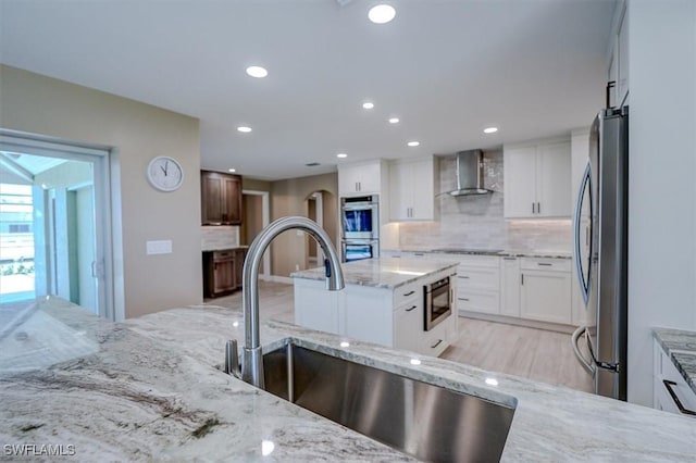 kitchen with light stone countertops, a sink, wall chimney exhaust hood, stainless steel appliances, and decorative backsplash