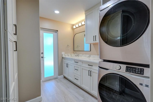 laundry room with cabinet space, a sink, baseboards, stacked washer / dryer, and light wood-type flooring