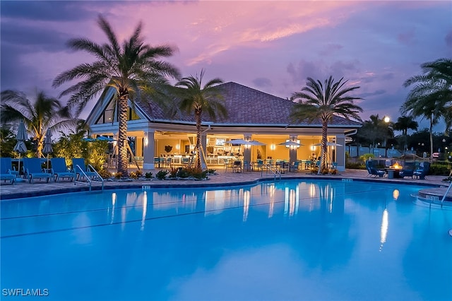 pool at dusk featuring a community pool and a patio