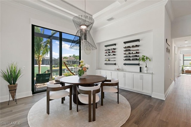 dining area featuring crown molding, an inviting chandelier, baseboards, wood finished floors, and visible vents