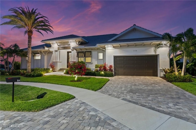 view of front of house featuring an attached garage, a front lawn, stucco siding, and decorative driveway