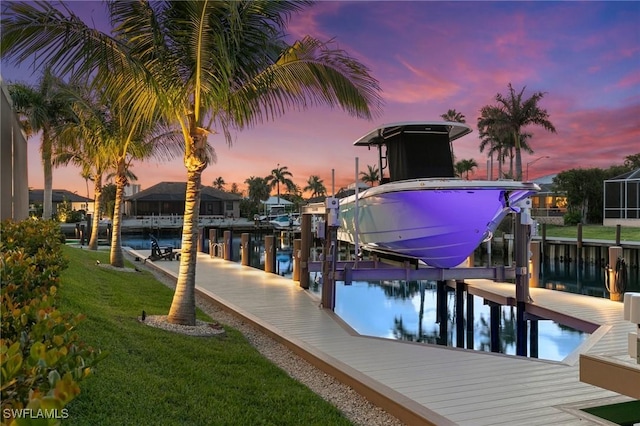 dock area with boat lift, a water view, and a yard
