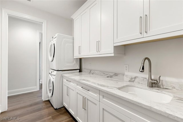 laundry area featuring wood finished floors, baseboards, stacked washing maching and dryer, a sink, and cabinet space