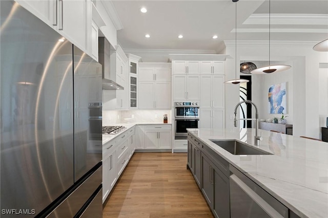 kitchen with crown molding, wall chimney range hood, white cabinetry, a sink, and appliances with stainless steel finishes