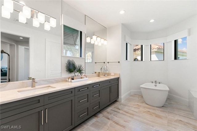 full bathroom featuring double vanity, a freestanding bath, a sink, and marble finish floor