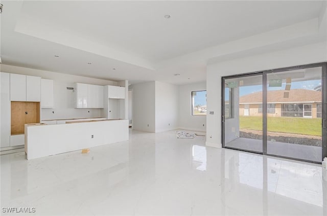 unfurnished living room featuring a raised ceiling and baseboards