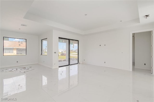 unfurnished room featuring a raised ceiling, plenty of natural light, and baseboards
