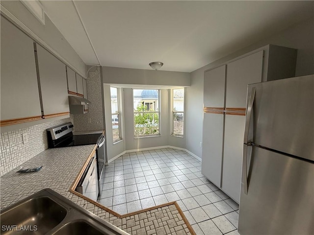 kitchen with a sink, stainless steel appliances, light tile patterned floors, tasteful backsplash, and under cabinet range hood