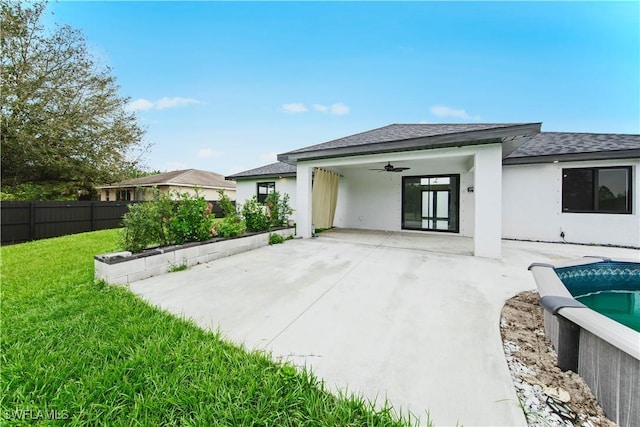 back of house featuring a ceiling fan, a lawn, fence, a shingled roof, and stucco siding