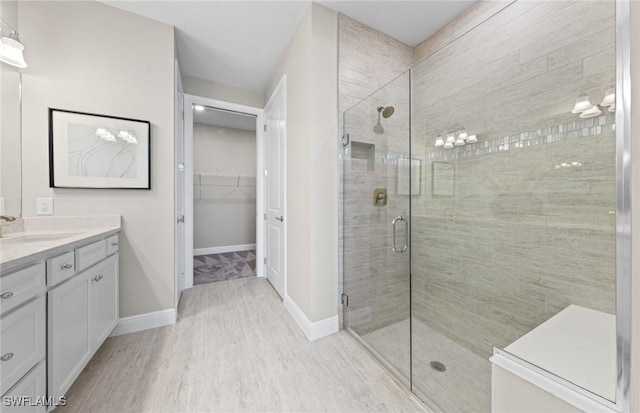 bathroom featuring a walk in closet, vanity, baseboards, a shower stall, and wood finished floors