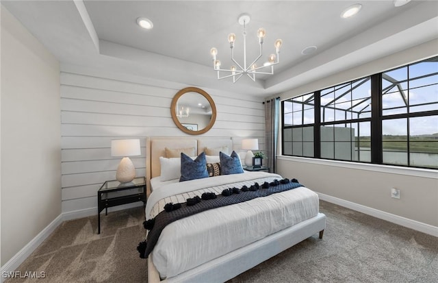 carpeted bedroom with a tray ceiling, a chandelier, and baseboards