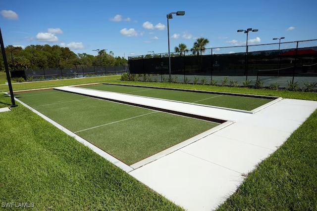 surrounding community featuring a lawn, fence, and a tennis court